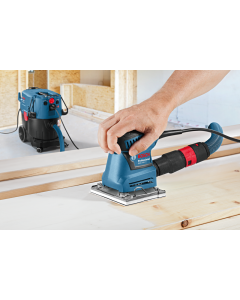 Bosch Professional GSS 140-1 A. A hand held sander being used on timber. Dust extractor attached to the rear. 