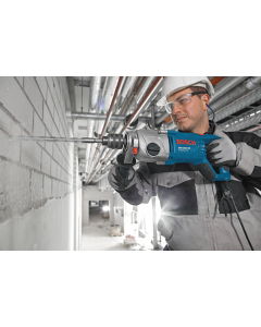 A man wearing a safety had and protective eyewear using a Bosch GSB 162-2 RE Impact Drill to drill into a wall. 