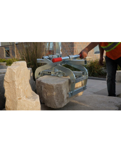 A person in a high-visibility vest using a Probst TSZ-UNI Block Gripper with red handles to move a natural stone boulder. 