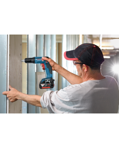 Man in a white sweatshirt, a black and red baseball cap and safety eyewear using a Bosch GSR 18V-EC TE Cordless Drywall Screwdriver.
