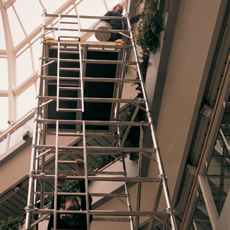 Man in navy overalls climbing an aluminium scaffold tower