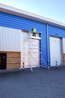 Man stood at the top of Single width Silver scaffold Tower maintaining frontage of industrial unit.